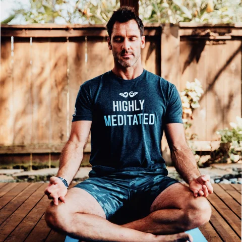 Andrew Schultz meditating on a yoga mat outdoors.