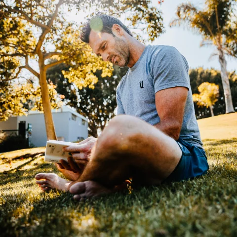 Andrew Schultz reading a book while sitting on grass outdoors.