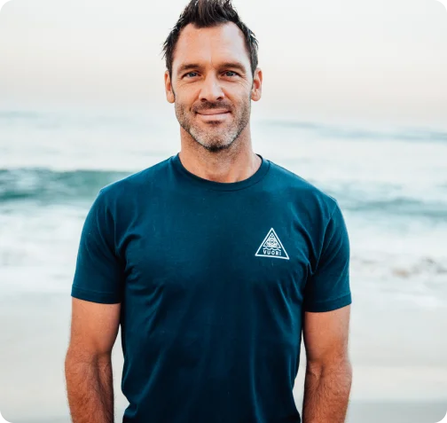 Andrew Schultz standing by the beach, smiling at the camera.