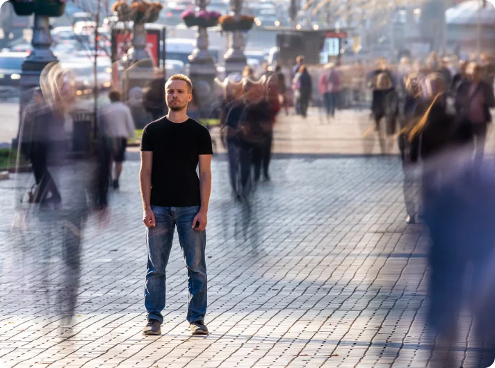 A man standing still on a busy city street, symbolizing the feeling of isolation amidst a crowd.