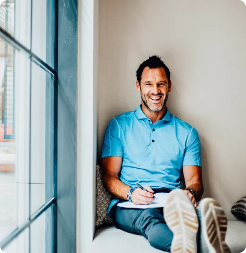 Andrew Schultz smiling and writing in a journal while sitting by a window