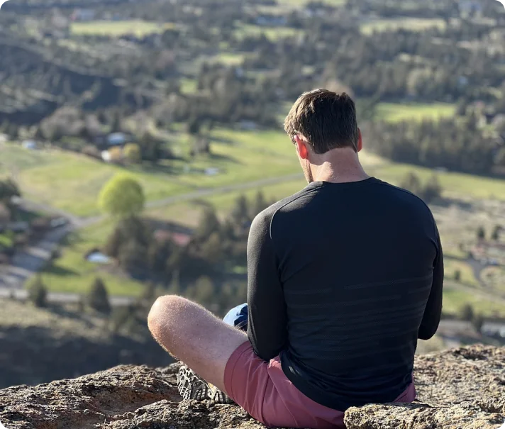 Man sitting on a cliff overlooking a scenic landscape